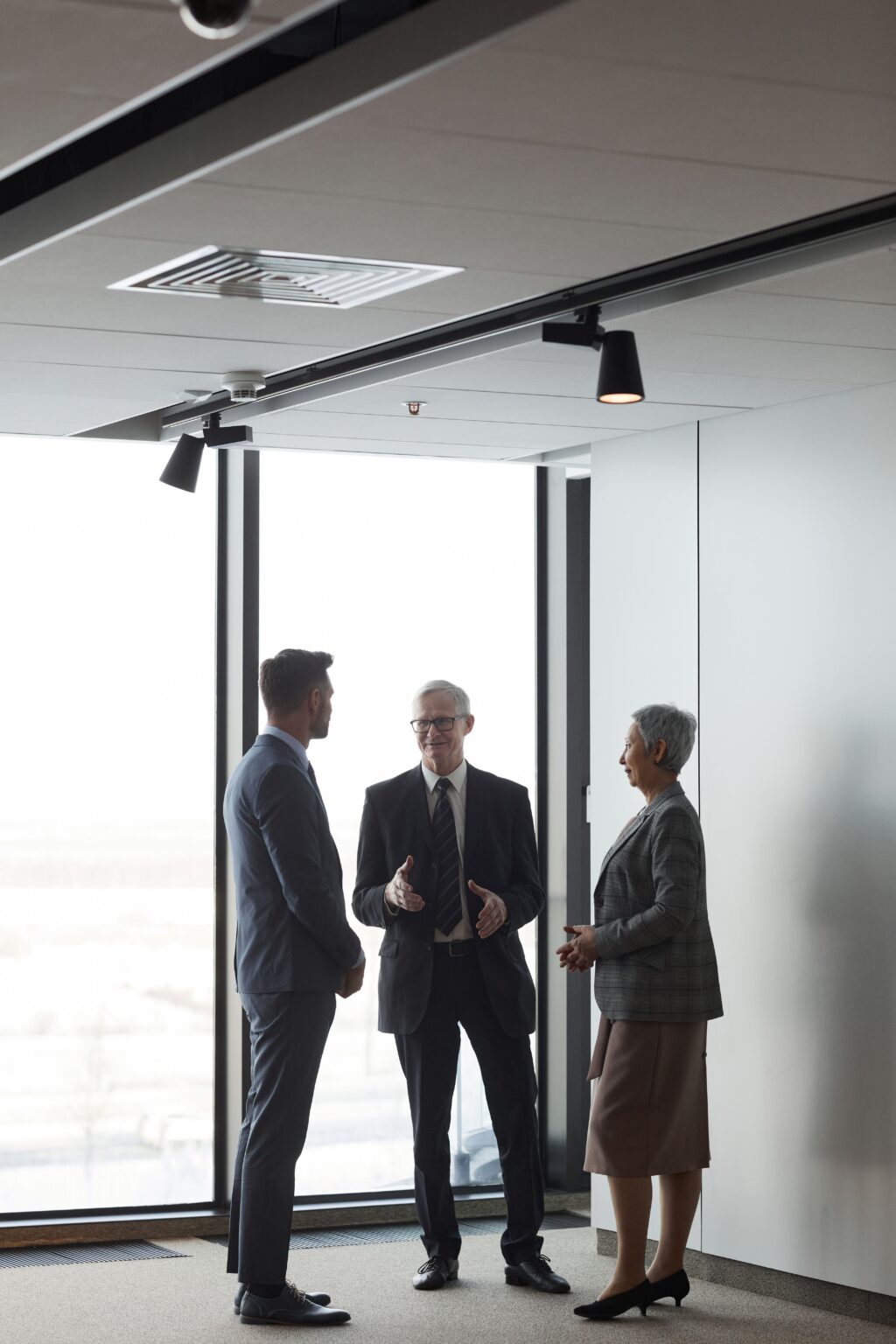 Senior business leaders in conversation beside a window in a corporate office
